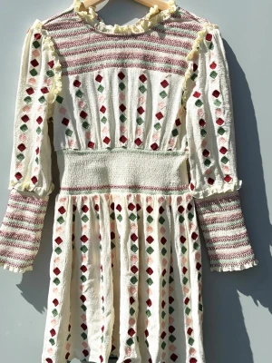 Vit långärmad klänning med mönster BY MALINA - Unik vit klänning med långa ärmar och broderade ränder samt rombformade detaljer i rött, grönt och rosa. Klänningen har volangdetaljer vid ärmslut och hals, samt en markerad midja för en feminin siluett. Perfekt för dig som gillar vintagevibbar och färgglada detaljer.                 