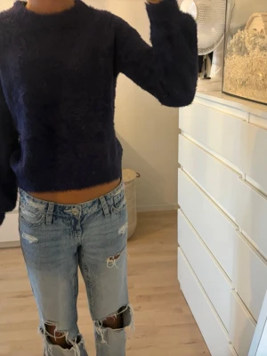 Mörkblå fluffig stickad tröja - Mysig mörkblå stickad tröja med fluffig textur och rund hals. Tröjan har långa ärmar och en enkel, rak passform.