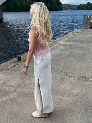 Vit långkjol med slits - Säljer en snygg vit långkjol med hög slits på sidan. Kjolen har en tight passform och är gjord i ett mjukt, stretchigt material som sitter skönt på kroppen. Perfekt för dig som vill ha en stilren och trendig look.