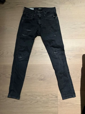 Svarta slitna slim fit jeans från replay  - Säljer slim fit replay jeans med slitningar och distressed detaljer på både fram- och baksida. Jeansen har klassisk femficksmodell, normal midja och är tillverkade i stretchigt denimtyg för en bekväm passform.