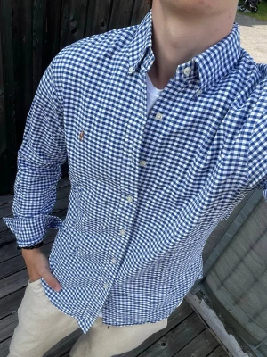 Blårutig skjorta från Polo Ralph Lauren - Säljer en blårutig skjorta från Polo Ralph Lauren i slim fit. Skjortan har klassisk button-down krage, vita knappar och det ikoniska broderade logot på bröstet. Tillverkad i mjuk bomull och perfekt för dig som gillar stilren och tidlös look.