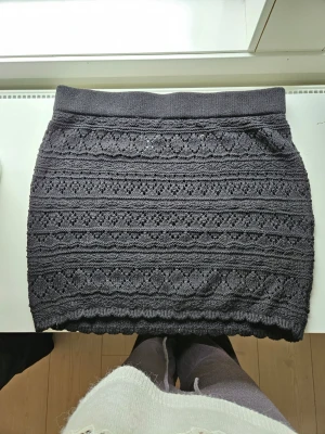 Mörkgrå stickad kjol från Divided - Säljer en svart stickat kjol med gullit mönster. Kjolen är perfekt att ha till stranden eller bara för en skön look. Oanvänd, hör av er för mer information