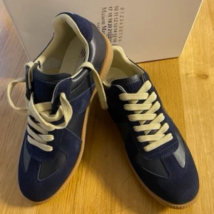Marinblå maisonmargela - Snygga marinblå sneakers med beige detaljer och vita skosnören. Ovandelen är i en mix av mocka och läder, och sulan är i gummi. Klassisk låg modell med retrovibbar och stilren design som passar till det mesta.