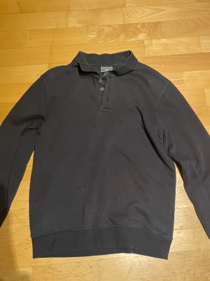 Svart långärmad pikétröja - Klassisk svart långärmad pikétröja med krage och knappar vid halsen. Tröjan har en enkel och stilren design, perfekt för en avslappnad men ändå snygg look. Tillverkad i mjukt material för extra komfort.