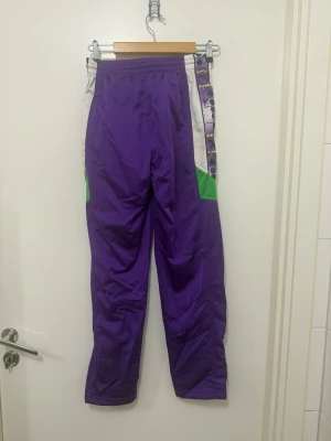 Sällsynta vintage 90-tals Diadora träningsbyxor Y2K stl M - Äkta retro 90-tals träningsbyxor från Diadora i unik färgkombination med lila, vitt och grönt. Snygga detaljer och i fint vintageskick. 100% polyester. 