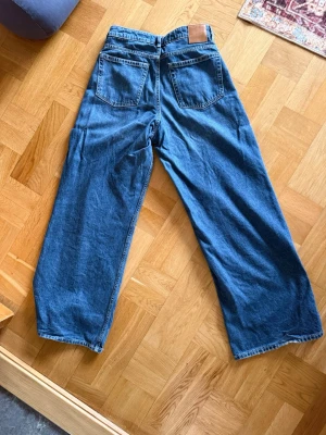 Blåa vida jeans med vida ben från bikbok, kerrie - Säljer ett par blåa jeans med bred passform och vida jeans.. Jeansen har klassiska fem fickor, medel hög midja och en snygg vintage-look. Tillverkade i denim med en cool, avslappnad stil som passar perfekt till streetwear eller casual outfits.