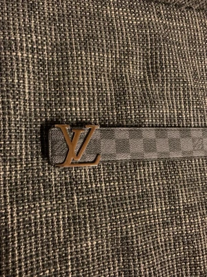  rutigt bälte i grått - Snyggt bälte med klassiskt rutigt mönster i grå och svart nyans. Bältet har ett stilrent spänne i metall och är tillverkat i skinn. Perfekt accessoar för att lyfta din outfit.
