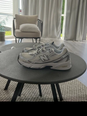 Vita New Balance 530 sneakers - Snygga vita New Balance 530 sneakers med silvriga och grå detaljer. Skorna har mesh- och syntetmaterial, klassisk N-logga på sidan och bekväm sula med ABZORB-dämpning. Perfekta för dig som gillar retrostil och sportig vibe.