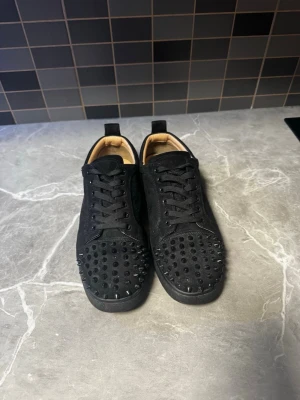 Christian Louboutin Louis Junior Spikes – Svarta - Säljer ett par stilrena Christian Louboutin Louis Junior Spikes i svart mocka med svarta spikes och den klassiska röda sulan. Skorna är använda men fortfarande i fint skick och passar perfekt för dig som vill ha ett exklusivt par sneakers till ett bra pris.