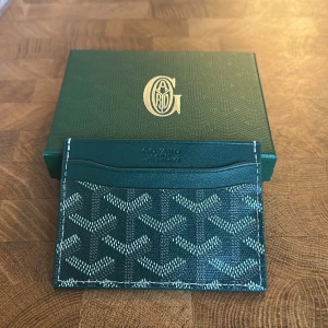 Goy4rd kortplånbok med mönster - Säljer en stilren grön kortplånbok från Goy4rd med deras ikoniska grafiska mönster i vitt och grått. Plånboken har flera kortfack och är tillverkad i exklusivt skinn med snygga kontrastsömmar. Perfekt för dig som vill ha något både lyxigt och praktiskt.