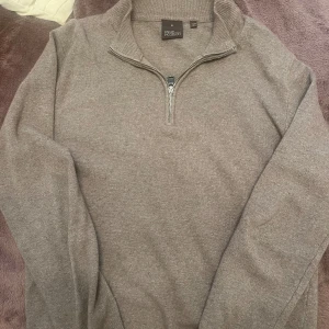 Beige stickad half zip från Oscar Jacobson - Snygg beige stickad tröja från Oscar Jacobson med half zip och hög krage. Perfekt för dig som gillar stilrena och klassiska plagg. Tröjan är långärmad och har en mjuk, skön känsla tack vare det stickade materialet. Passar dig som vill ha en clean look.