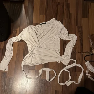 Vit omlottopp med långa ärmar - Snygg vit omlottopp med långa ärmar och knytband i midjan. Tunn och mjuk, perfekt för lager-på-lager eller att styla med jeans. V-ringad och figurnära passform som ger en clean och fräsch look.