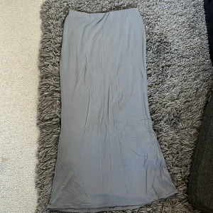 Grå långkjol från Bik Bok - En stilren grå långkjol från Bik Bok i mjukt och lätt material. Kjolen har en rak och enkel passform som faller snyggt längs kroppen. Perfekt att matcha med en crop top eller stickad tröja för en chill look.