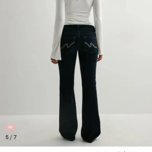 Mörkblå bootcut jeans med kontrastsöm - Snygga mörkblå jeans med bootcut passform och vita kontrastsömmar. Klassisk femficksmodell med låg midja och markerade bakfickor med broderad detalj. 