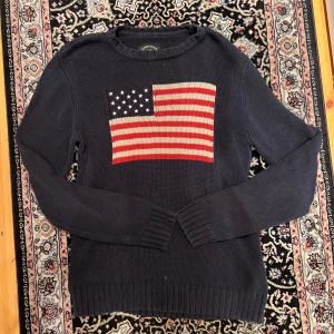 Ralph lauren flagg tröja liknande (crocker) - Mörkblå stickad tröja från Crocker i storlek M. Tröjan har ett stort amerikanskt flaggmotiv. Säljer för passade ej mig.