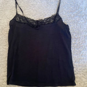 Svart spetstopp från Twilfit  - Svart linnetopp från Twilfit Change Lingerie med tunna axelband och vacker spetsdetalj längs urringningen. Snygg och enkel modell som passar perfekt till jeans eller kjol. Mjuk och följsam känsla.