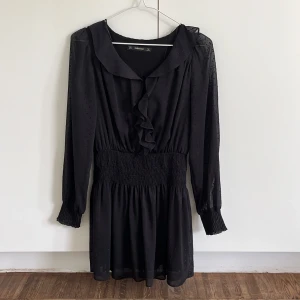 Svart kort klänning från Zara Basic - Supersöt svart kort klänning från Zara Basic med volangdetaljer framtill, prickigt mönster i tyget och smockad midja. Shorts på insidan.