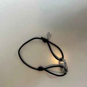 Valentino svart armband med silverdetalj - Snyggt armband från Valentino med svart justerbart band och en stilren silverfärgad logga i metall. Perfekt accessoar för att lyfta din outfit med en lyxig touch. Diskret bricka med Valentino-gravyr vid knuten. Kvitto från Farfetch tillgängligt