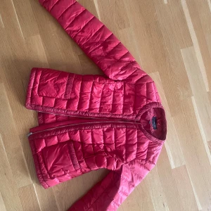 Röd pufferjacka med dragkedja - Säljer en röd pufferjacka från massimo dutti Jackan har två stora  framtill och stängs med dragkedja. Lätt och smidig modell som är perfekt till hösten. Passformen är normal och lite figursydd.