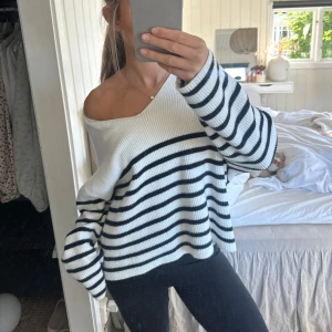 Stickad tröja randig  - Säljer en vit och marinblå randig stickad tröja med oversized passform. Tröjan har långa ärmar, bred v-ringning och kan bäras offshoulder för en chill vibe. Perfekt till jeans eller leggings för en avslappnad look.