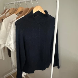 Mörkblå stickad polotröja - Mysig mörkblå stickad polotröja med hög hals och lång ärm. Perfekt för kyliga dagar och enkel att matcha med jeans eller kjol. Tröjan har en rak passform och är superbekväm att bära.