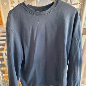 Mörkblå sweatshirt från H&M - En enkel och stilren mörkblå sweatshirt från H&M i relaxed fit. Tröjan har rund hals, långa ärmar och ribbade muddar vid hals och ärmslut. Perfekt för chill dagar och passar till jeans eller mjukisbyxor. Materialet är mjukt och skönt, troligen bomull och polyester.