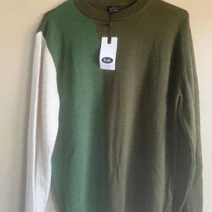 stickad tröja - Snabb leverans! Tröjan har aldrig blivit använd, är helt ny!! Snygg stickad tröja från F&K i storlek M. Tröjan har en cool färgblock-design med olivgrönt, mörkgrönt och en vit ärm. Rund halsringning och långa ärmar. Perfekt för dig som gillar en unik och stilren look.