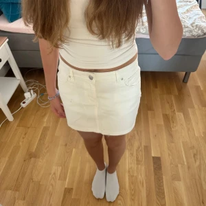 Vit jeanskjol  - Snygg vit jeanskjol jag tror att den är från Bik bok  med klassisk femficksdesign, bälteshällor och knapp framtill. Kjolen är kort och har raka linjer, perfekt till sommaren. Materialet är stadigt denim i bomull och passformen är normal. 