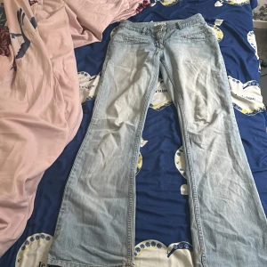 Ljusblå bootcut jeans - Säljer ett par ljusblå jeans med bootcut passform. Jeansen har klassisk femficksdesign, dragkedja och knapp framtill. Perfekta för dig som gillar en retroinspirerad stil med utsvängda ben.