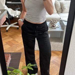 Svarta satinbyxor med snörning - Svarta satinbyxor med bred resår i midjan och snörning framtill. Byxorna har raka ben och sidfickor, vilket gör dem både sköna och stilrena. Perfekta för en chill vardagslook eller när du vill vara bekväm men ändå se snygg ut. Lite tjockare tyg så ser lyxiga ut! Älskar dom men har tyvärr blivit för små😢