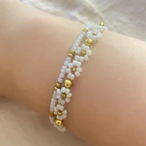 Pärlarmband med blommor i vitt och guld - Två handgjorda pärlarmband med små vita pärlor och guldfärgade detaljer. Ett armband har söta blommor av pärlor med guldfärgade pärlor i mitten, det andra är enkelt med vita och guldfärgade pärlor. Perfekt för dig som gillar unika och söta accessoarer.