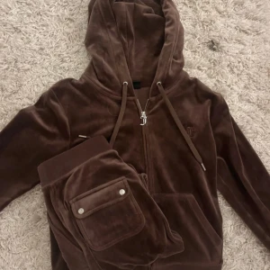 Brunt Juicy Couture sett - Mysig brun hoodie från Juicy Couture i mjuk velour med dragkedja, snörning i huvan och broderad logga på bröstet. Perfekt för chill dagar och har en klassisk, avslappnad passform. Säljes i storlek S.