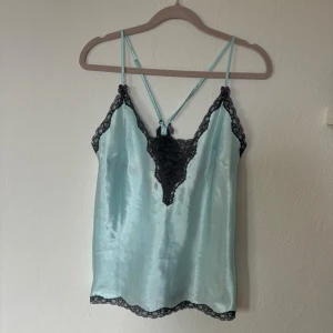 Satin linne med spets  - Ljusblå/turkost satin linne med spetskanter och spets vid bröstet. På banden sitter rosetter både fram och bak. Den har små glitterstenar vid spetsen. Axelbanden är justerbara.  Skriv om du har några frågor🩷