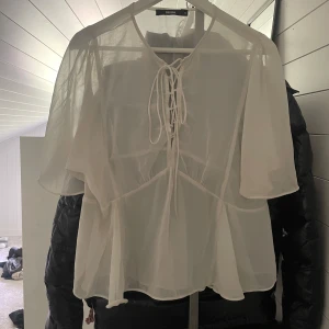 Vit transparent blus från Bik Bok - Superfin vit blus från Bik Bok i transparent, luftig polyester. Blusen har vida, korta ärmar och snygg snörning framtill som ger en trendig look. Perfekt att styla lager på lager eller med ett linne under. Lätt och flowy känsla.