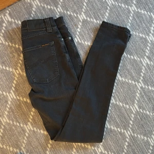 Svarta Nudie Jeans - Hej 👋 | Säljer ett par svarta jeans från Nudie Jeans i klassisk slim modell. Perfekt för dig som e runt 165 Jeansen har fem fickor, svarta sömmar och en diskret logga på bakfickan. Perfekta för dig som gillar stilrena och tidlösa jeans med snygg passform. Skriv vid intresse 🤝