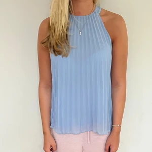 Ljusblå plisserad ärmlös linnetopp - Superfin ljusblå linnetopp med plisserat tyg och hög hals. Toppen är ärmlös och har en flowy passform.