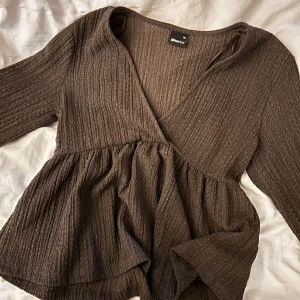 Brun V-ringad topp från Gina Tricot XS - Mysig brun V-ringad topp från Gina Tricot i storlek XS. Toppen har lång ärm, v-ringning och volangliknande nederdel samt vid armarna. Materialet är ribbat och ger en snygg struktur. Perfekt för hösten. Använd endast en gång. Nypris:449kr. Hör av er vid frågor 💓