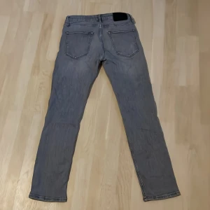 Grå jeans från Jack & Jones - Snygga grå jeans från Jack & Jones med klassisk femficksdesign och raka ben. Jeansen har en cool tvättad look och är tillverkade i mjukt denimtyg som sitter skönt hela dagen. Perfekta till sneakers och hoodie för en avslappnad stil.