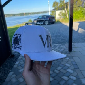 Vit Vonroe keps med brodyr - Snygg vit keps från Vonroe Collective med grå broderad VR-logga framtill och detaljerad brodyr på sidan. Storleken är 57.7 centimeter. Nypris 500kr