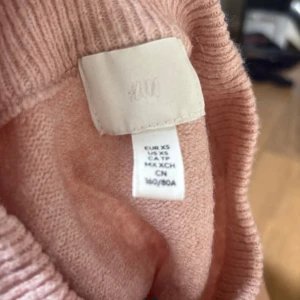 Ljusrosa stickad tröja från H&M - Mysig ljusrosa stickad tröja från H&M i storlek XS. Tröjan har rund halsringning, ribbade muddar och är långärmad. Perfekt för lager-på-lager och chill dagar. Enkel och stilren design som funkar till det mesta.