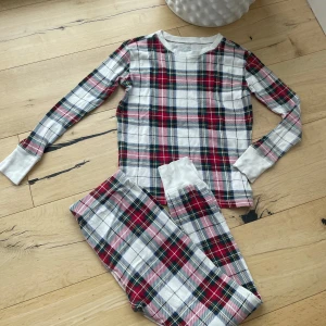 Rutig pyjamas  från GAP - Snygg långärmad pyjamas  från GAP i röd, vit och blå rutig design. Tillverkad i mjuk ekologisk bomull, perfekt för mysiga dagar. Tröjan har rund halsringning och breda muddar vid ärmsluten för extra komfort. Köpt på Zalando