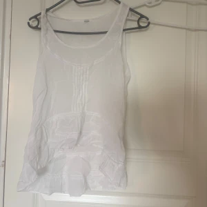 Vit ärmlös linnetopp med spetsdetaljer - Säljer en söt vit linnetopp med spetsdetaljer vid axelbanden och dekorativa sömmar framtill. Toppen är ärmlös och har en luftig känsla, perfekt för varma dagar🌻🌻☀️
