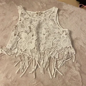 Vit spetsig croppad linnetopp H&M Coachella - Superfin vit croppad linnetopp från H&M Coachella-kollektionen. Toppen är i spets med stora blommiga mönster och har snygga fransar längst ner. Perfekt för festival eller sommarhäng, riktigt boho-vibe!