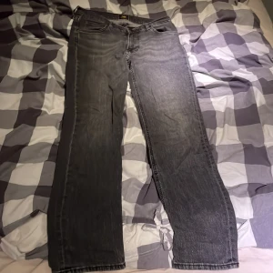 Grå Lee jeans W30 L32 straight fit - Säljer ett par grå jeans från Lee i modellen West, storlek W30 L32. Jeansen har klassisk femficksdesign, raka ben och normal passform. Materialet är bomull med en snygg tvättad look. Perfekta för dig som gillar en enkel och stilren vibe.