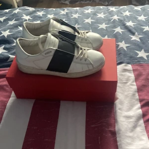 Valentino Garavani Open sneakers vit/svart - Säljer ett par Valentino Garavani Open sneakers i vitt skinn med bred svart läderdetalj över vristen. Klassisk rund tå, snörning och ikoniska nitar på hälen. Snygg och stilren design som sticker ut med kontrastfärger. Kvitto, box och dustbag medföljer! Går att förhandlas
