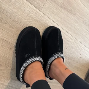 Svarta UGG mocka boots med mönsterkant (tazman) - Svarta boots från UGG i mjuk mocka med fluffigt foder och kraftig platt sula. Skorna har en snygg vit och svart mönstrad kant upptill som ger en unik touch. Endast använda 2 gr pga att dem är lite små.