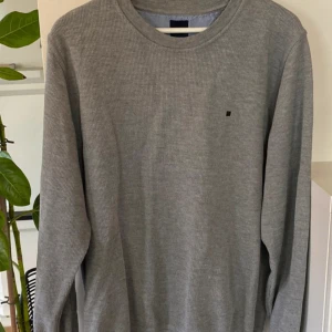 Tröja från Redgreen! M -  Säljer en stilren grå långärmad tröja från Redgreen med diskret logga på bröstet. Tröjan har rund halsringning och är ribbad i materialet, vilket ger en snygg struktur. Perfekt för lager-på-lager eller som den är.Tröjan är i jättefint skick, inga skador, noppror eller anmärkningar. Intresserad? Fler bilder? Hör av dig!