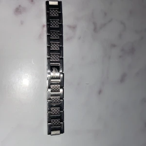 Silvrigt  armband Lacoste  - Säljer ett silvrigt armband från Lacoste Länken är i metall med snyggt rutmönster på varje länk och klassisk design. Perfekt om du vill byta ut ditt gamla armband och ge dig själv en fräsch look.