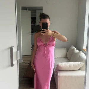 Rosa långklänning med öppen rygg - Säljer en superfin rosa långklänning med smala axelband och snygg öppen rygg. Klänningen har en söt knytning framtill och är figurnära med mjukt fall. Perfekt för sommarkvällar eller när du vill känna dig extra söt! 💖
