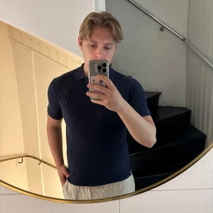 Marinblå pikétröja från Ralph Lauren - Säljer en klassisk marinblå pikétröja från Ralph Lauren i storlek L. Tröjan har korta ärmar, krage och knappar framtill. Tillverkad i 100% bomull och har den ikoniska broderade loggan på bröstet. Perfekt för en clean och stilren look. Sitter som XS/S